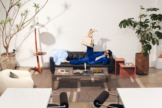 woman sitting on a couch with a bag hanging off of her leg in an editorial style picture