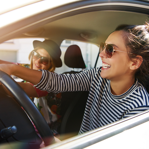 Carefree laughing young girls in sunglasses driving a car, looking out the window