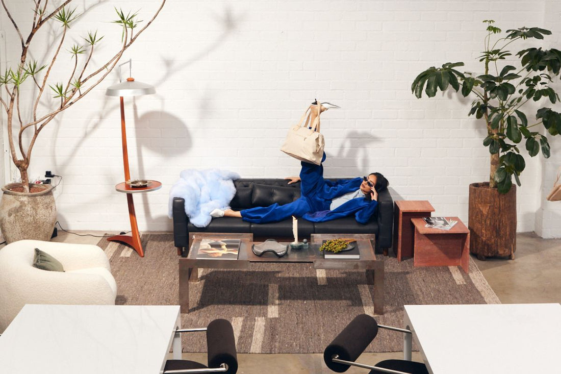 woman sitting on a couch with a bag hanging off of her leg in an editorial style picture