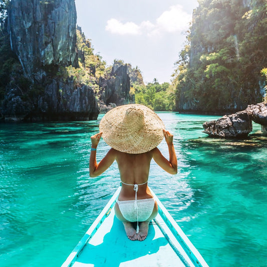 Back view of the young woman in straw hat relaxing on the boat and looking forward into lagoon